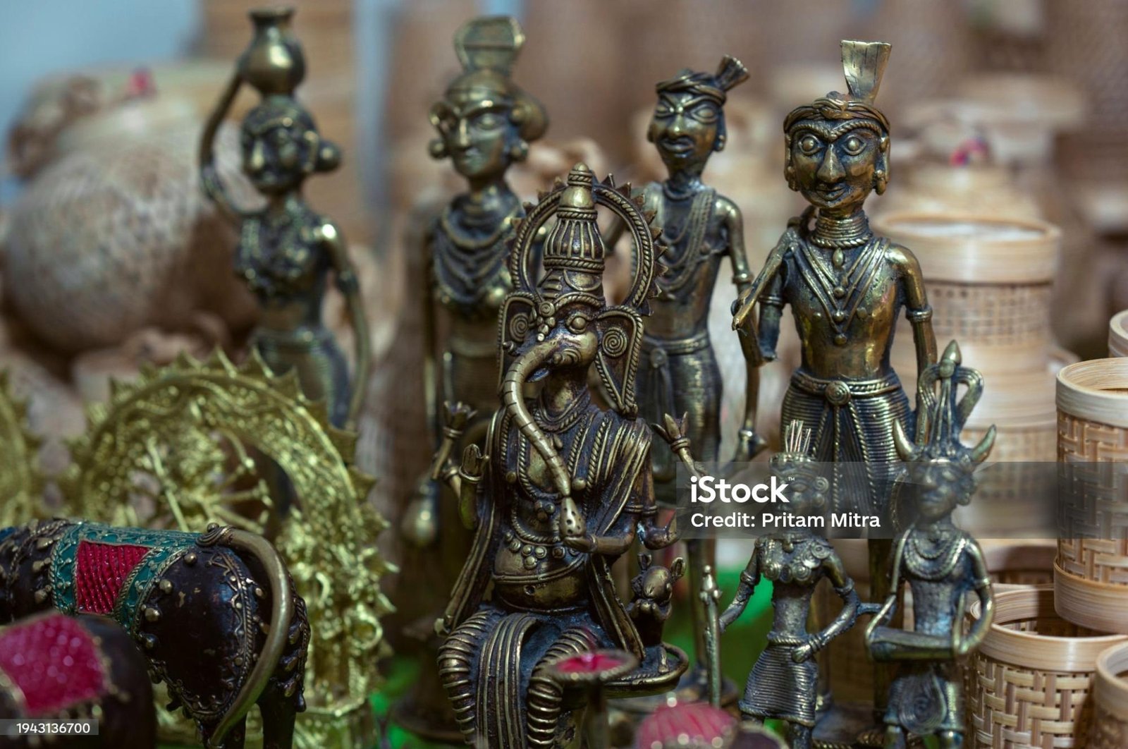 Traditional Indian brass figurines, including a seated Lord Ganesha idol and tribal-style human figures, displayed in a handicraft shop surrounded by intricately designed bamboo and wooden artifacts.